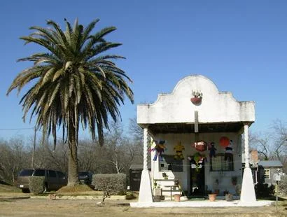 Small white building beside a tall palm tree in Natalia, Texas